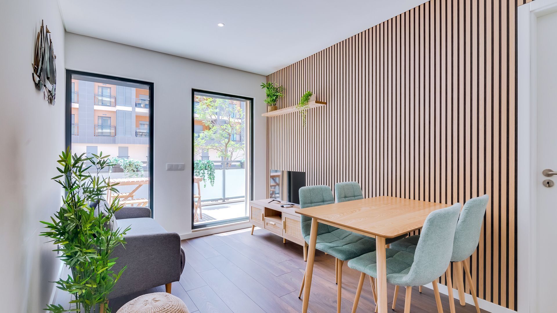 A modern dining area with a wooden table and chairs, a sofa, and a view of the outside through large windows.