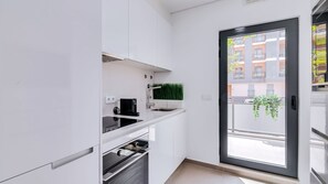 A modern kitchen with white cabinets, a black stove, and a window with a view of buildings and greenery.
