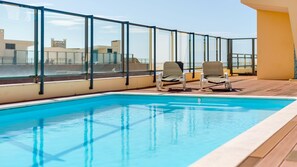 A rooftop pool with two lounge chairs and a glass balustrade.