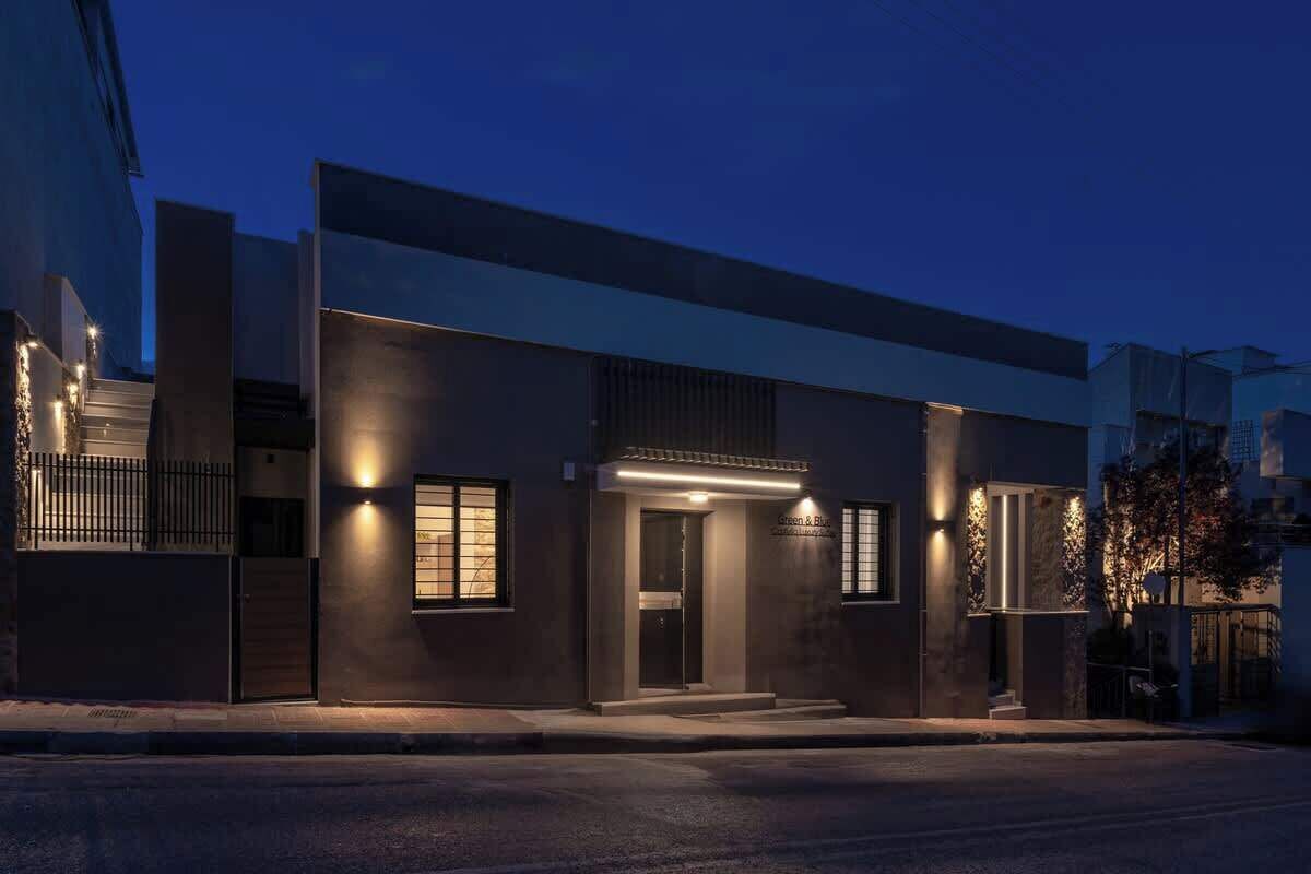 Un bâtiment moderne à la façade sombre, doté d’une entrée illuminée et d’une plaque signalétique bien visible.