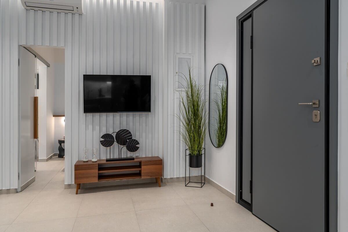 A modern living room with a flat-screen TV, a wooden console, a potted plant, and a door.