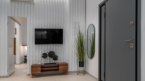 Een moderne woonkamer met een flatscreen televisie, een houten dressoir, een kamerplant en een deur.