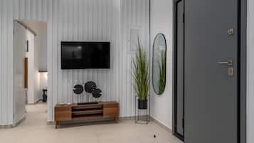 A modern living room with a flat-screen TV, a wooden console, a potted plant, and a door.