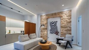 Een moderne woonkamer met een bank, salontafel en stoelen, een accentmuur van steen en een keuken met kasten en een aanrecht.