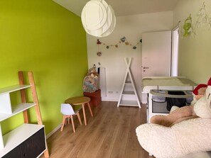 Habitación infantil con cama, una mesita, una silla, una escalera y un mueble para guardar cosas.