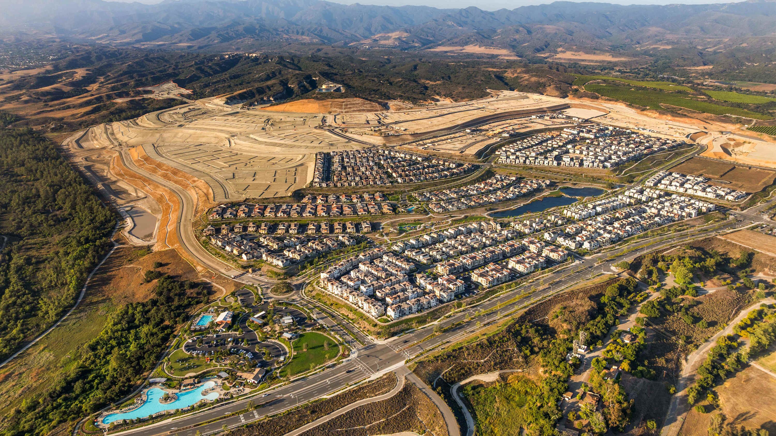 An aerial view of a residential area with a large, organized layout of houses, a swimming pool, and a road network.