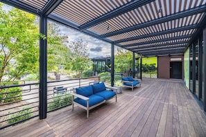 An outdoor deck with wooden flooring, blue sofas, and a glass railing overlooking a garden.