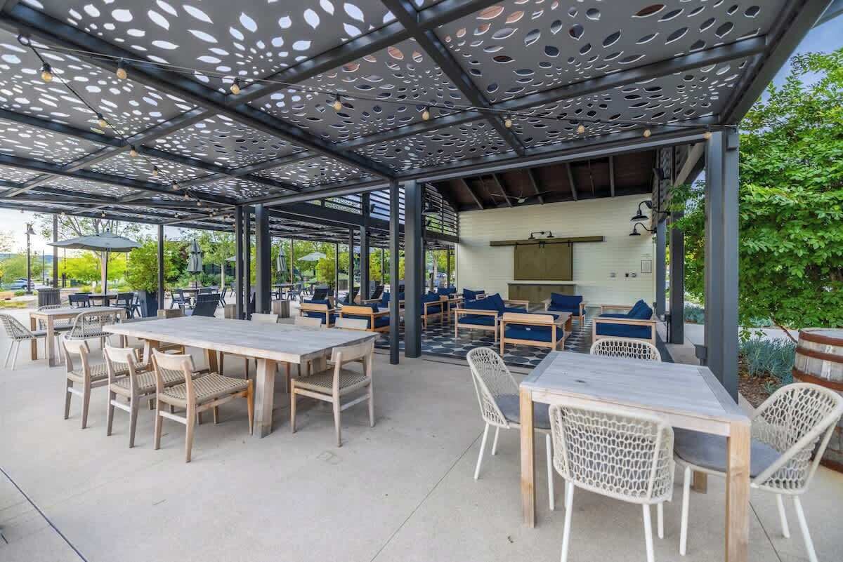 An outdoor patio with wooden tables and chairs, a covered seating area, and a grill.