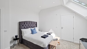 Une chambre à coucher avec un grand lit, une table de chevet, une chaise, un bureau, une armoire, un puits de lumière et une porte.