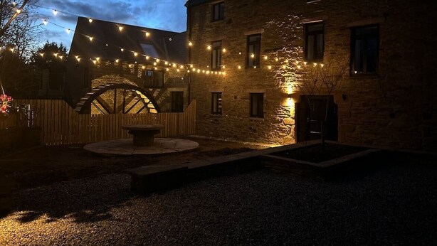Un bâtiment en pierre doté d’une roue à eau, de guirlandes lumineuses et d’une clôture en bois.