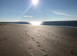 Ranta, jossa näkyy jalanjälkiä, kirkas taivas ja aurinko paistaa.