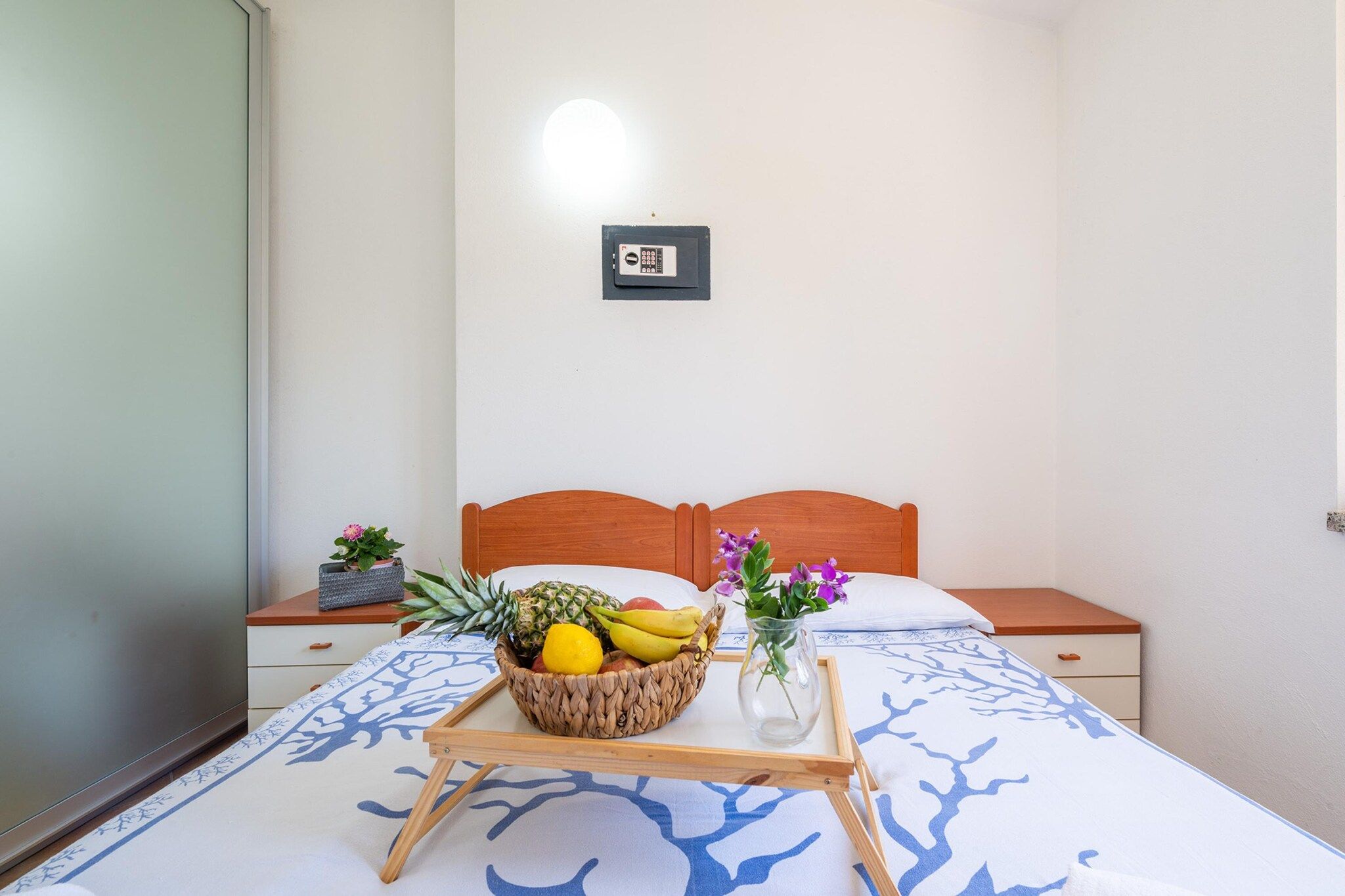 A bedroom with a bed, a bedside table, a nightstand, a wall-mounted light, and a framed picture.