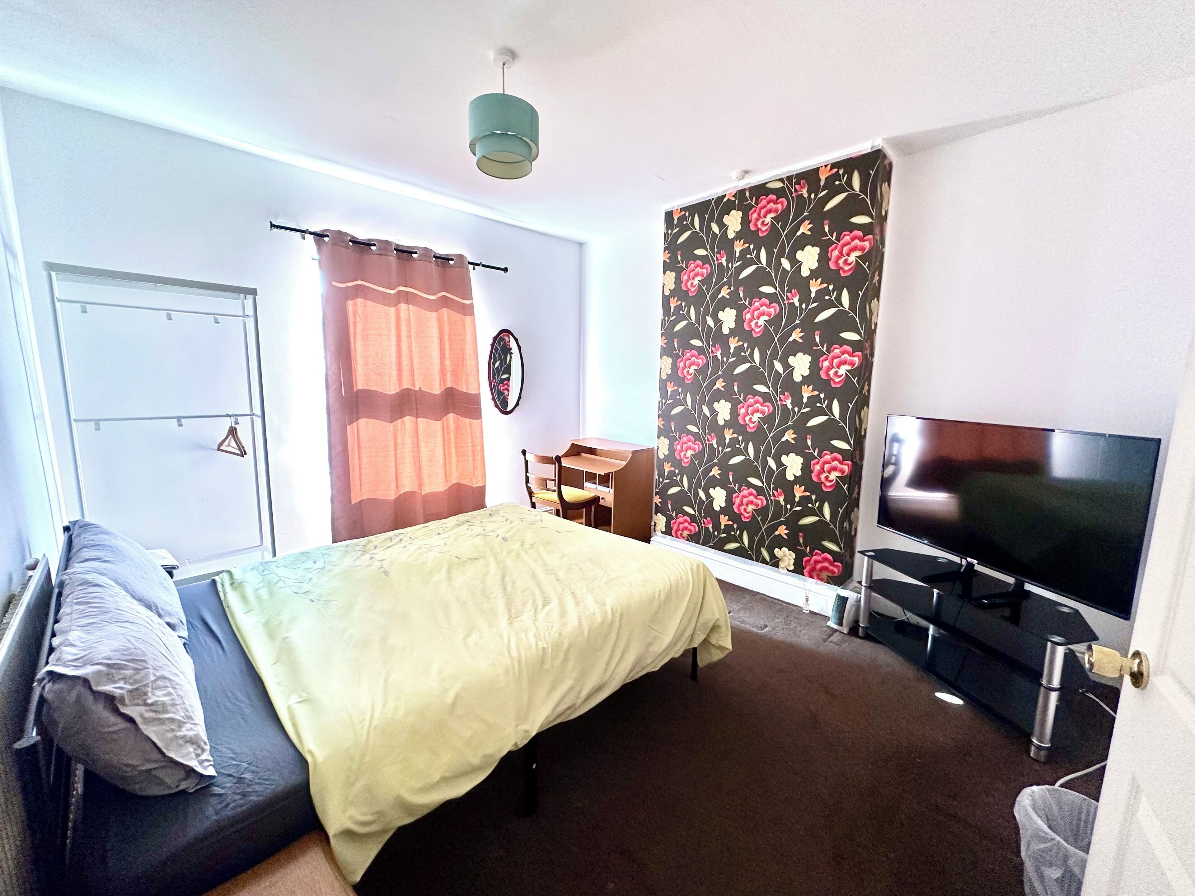 A room with a bed, a desk, a TV, and a window with curtains.