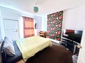 Ein Zimmer mit Bett, Schreibtisch, Fernseher und einem fenster mit Vorhängen.