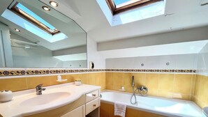 Une salle de bain avec un puits de lumière, un lavabo, une baignoire et des toilettes.