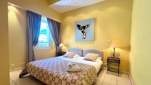 Une chambre d’hôtel avec un grand lit, deux tables de chevet, une fenêtre avec des rideaux, une œuvre d’art accrochée au mur et une lampe.
