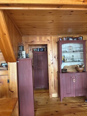 A wooden interior with a door, cabinets, and a shelf with glassware.