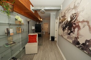 A modern hallway with a glass display unit, a white sofa with a red cushion, and a large abstract painting on the wall. - City-Chic at Centennial Hill downtown (Atlanta)