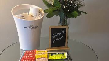 Una mesa de vidrio con un letrero de bienvenida, un ramo de flores, un balde con la etiqueta 'MOËT & CHANDON CHAMPAGNE' y varios paquetes de té y especias.