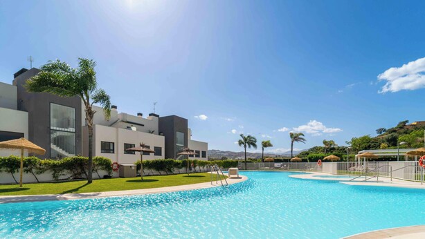 Una piscina con cielo azzurro limpido, edifici moderni e palme.