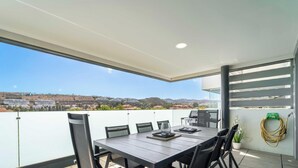 Un balcone con tavolo, sedie, barbecue e un tubo da giardino.
