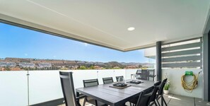 Ein Balkon mit Esstisch, Stühlen, Grill und Gartenschlauch.