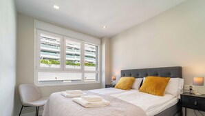 Una camera d'hotel con un letto, due lampade sui comodini, una sedia, una finestra con vista su un edificio e un tavolino.