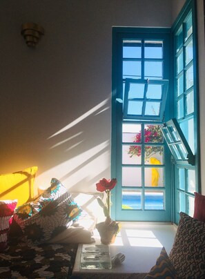 Ein Zimmer mit einem blauen Fenster, einem Blumentopf und gemusterten Kissen.