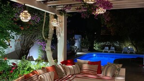 Uma área de estar coberta ao ar livre com uma piscina ao fundo.
