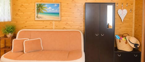 A cozy room with a wooden interior, a sofa, a wardrobe, a small table with a plant, and a wall-mounted picture of a beach.