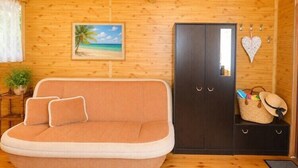 A wooden cabin interior with a sofa, a wardrobe, a heart-shaped decoration, and a beach-themed painting. - Cottage for 4 people, Wapnica (Wapnica)