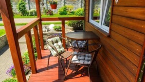 A wooden deck with two chairs and a small table, a stone wall with greenery, and a window with a view. - Cottage for 4 people, Wapnica (Wapnica)