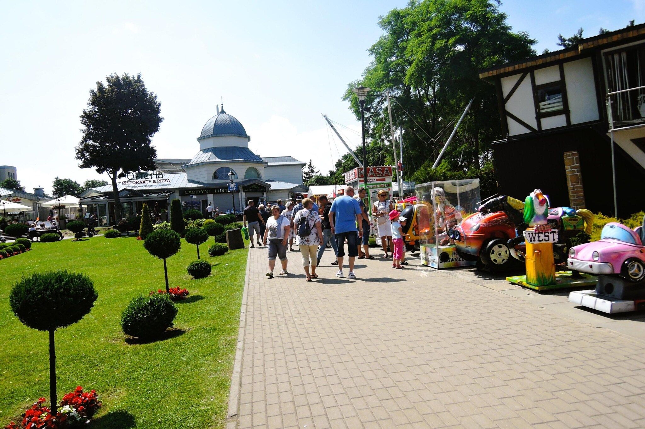 A paved walkway with people walking, a building with a dome, and a colorful car display.