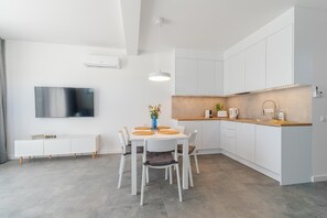 A modern kitchen with white cabinetry, a dining table with chairs, a TV mounted on the wall, and a pendant light.