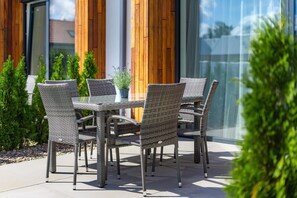 En udendørs terrasse med fletmøbler og en glasdør.