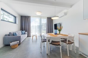 En moderne stue med sofa, spisebord, stole, et fjernsyn og et vindue med gardiner.
