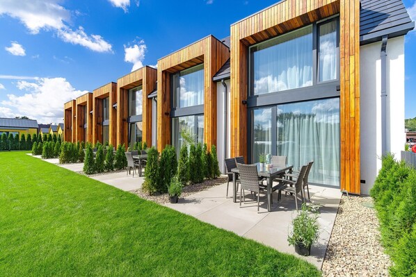 A modern building with large windows and wooden accents, a well-maintained lawn, and outdoor seating.