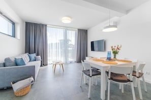 A modern living room with a sofa, dining table, chairs, and a TV.