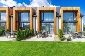 A modern building with large windows and wooden accents, outdoor seating, and a well-maintained lawn.