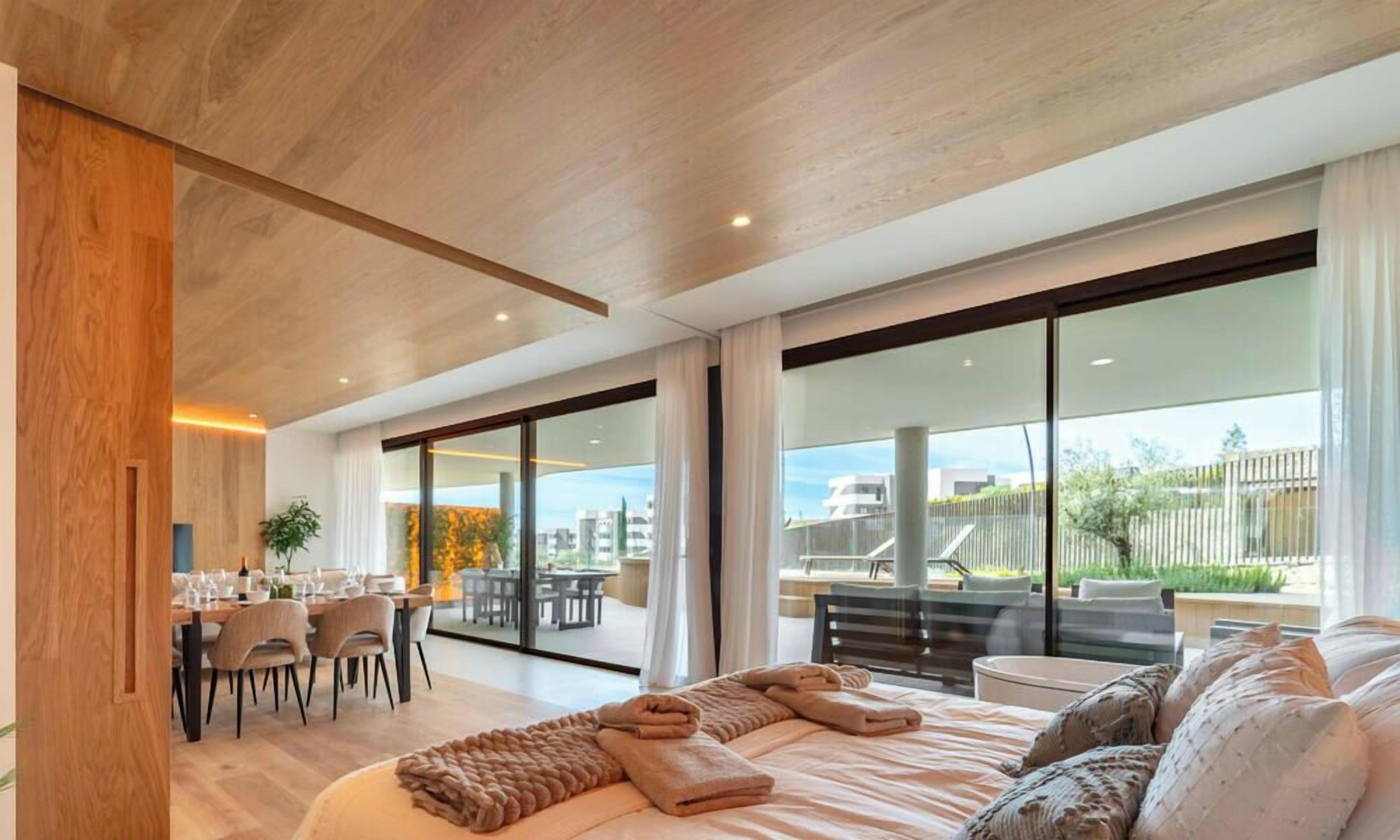 A modern hotel room with a large bed, a dining area, and a balcony with a view.