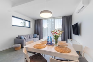 Un salon moderne avec un canapé, une table à manger avec des sets de table, un vase de fleurs et un téléviseur à écran plat fixé au mur.