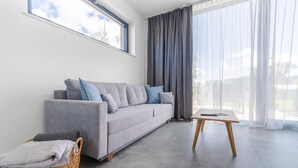 Un saló modern amb un sofà gris, una taula de fusta petita, una cistella de vimet i un finestral gran amb cortines.