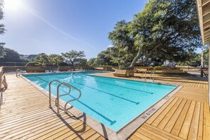 Ein Schwimmbecken mit einer Holzterrasse, umgeben von Bäumen und einem Zaun.