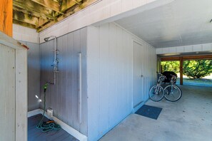 Ein überdachter Außenbereich mit Dusche, einem Fahrrad und einer zur Gebäudetür führenden Öffnung.