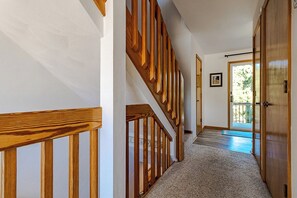A hallway with wooden railings, a carpeted floor, and a door leading to an outdoor area. - Sun Realty oceanside townhome w/ community pool & beach access (Duck)