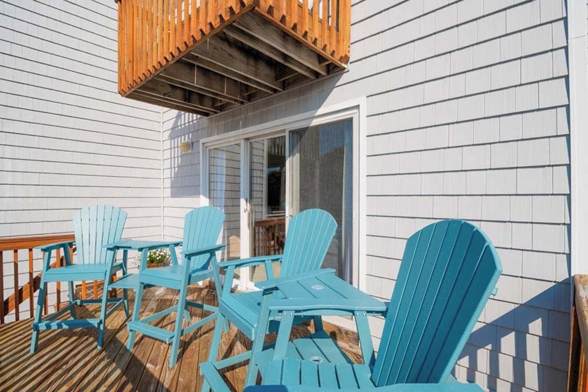 A deck with blue Adirondack chairs and a wooden railing.