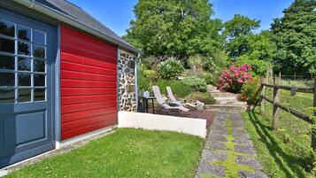 A red building with a stone facade, a stone pathway, and a garden with a wooden fence.