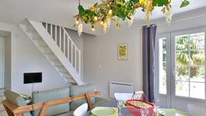 Un coin repas avec une table dressée pour quatre personnes, un canapé, un escalier et une fenêtre donnant sur un paysage verdoyant.