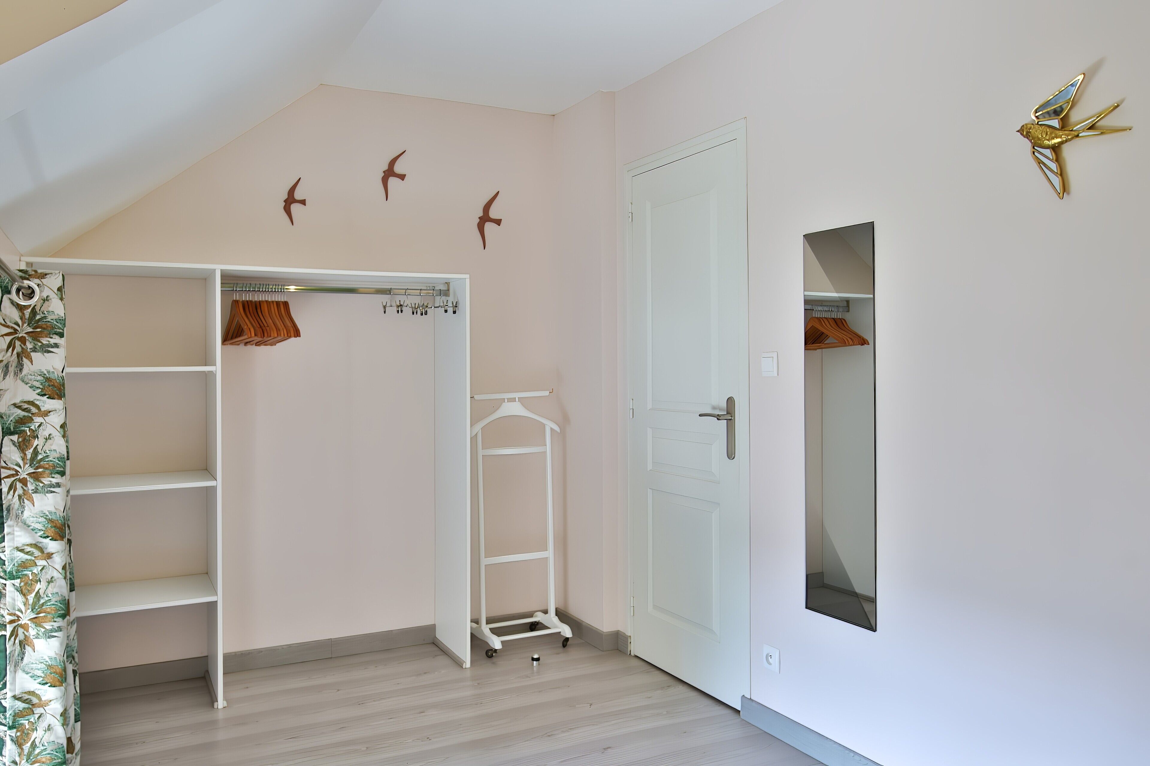 Una habitación con un armario blanco, piso de madera y una puerta con espejo.