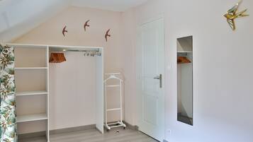 Una habitación con un armario blanco, piso de madera y una puerta con espejo.